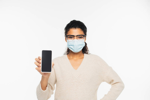 Donna afroamericana in occhiali e maschera medica con cellulare con schermo bianco isolato su bianco - Foto, immagini