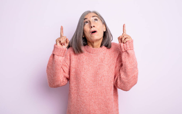 Senior hübsche Frau sieht schockiert, erstaunt und mit offenem Mund, zeigt mit beiden Händen nach oben, um Raum zu kopieren - Foto, Bild