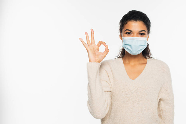 Young african american woman in medical mask showing okay gesture isolated on white - Fotó, kép