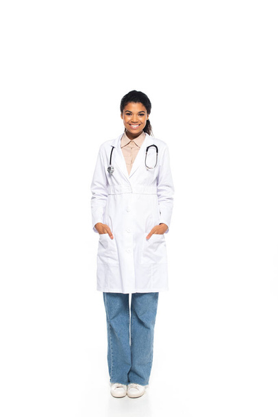 Teljes hossza mosolygós afro-amerikai orvos sztetoszkóppal nézi kamera fehér háttér  - Fotó, kép