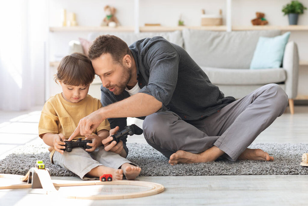 Junger Papa erklärt kleinem Sohn, wie man mit Steuerknüppel spielt, bringt seinem Kind bei, Videospiele zu spielen, gemeinsam Spaß zu haben - Foto, Bild