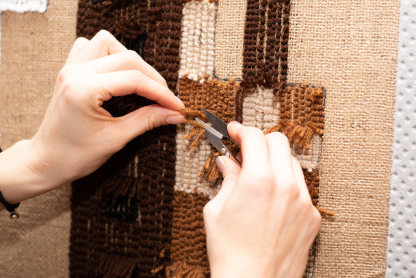 A szőrtelenítő szőnyeg készítésének folyamata. Varró olló női kezekben a háttérben egy kézzel készített barna tartály szőnyeg zsákba. - Fotó, kép