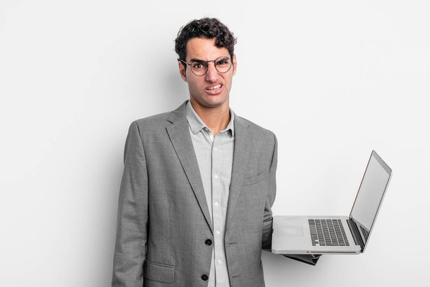 hispanic handsome man feeling puzzled and confused. business and laptop concept - 写真・画像