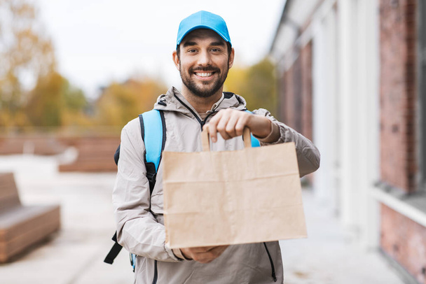 happy delivery man with takeaway food in paper bag - Фото, изображение