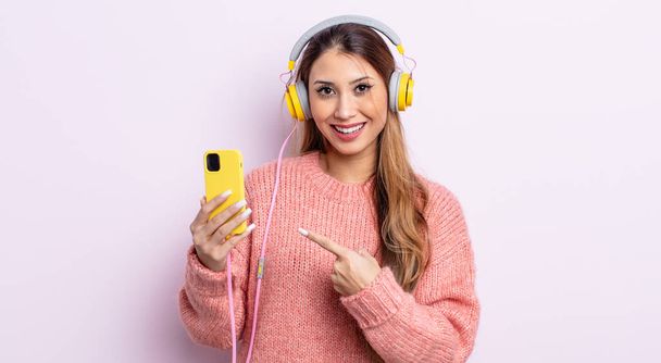 asiatic pretty woman looking excited and surprised pointing to the side. headphones and phone concept - Foto, Bild