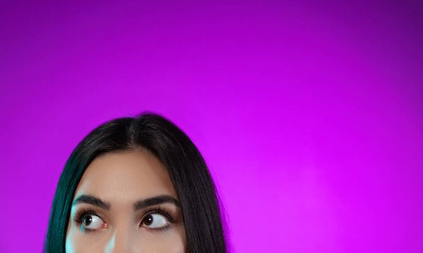 Imagen recortada de hermosos ojos femeninos mirando lado izquierdo aislado sobre fondo púrpura - Foto, Imagen
