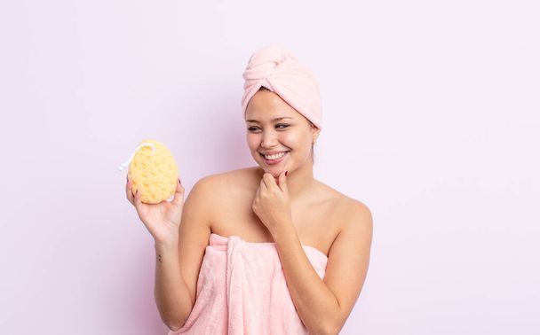 hispanic pretty woman smiling with a happy, confident expression with hand on chin. bathrobe and sponge concept - Foto, Bild