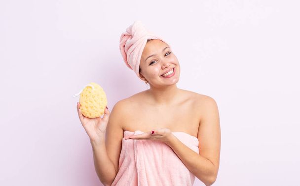 hispanic pretty woman smiling cheerfully, feeling happy and showing a concept. bathrobe and sponge concept - Fotó, kép