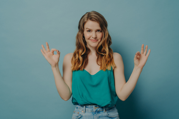 Sebevědomá radostná mladá žena v neformálním oblečení gestikuluje ok znamení s oběma rukama ve studiu - Fotografie, Obrázek