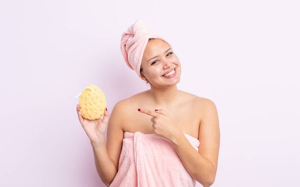 spanyol csinos nő vidáman mosolyog, boldognak érzi magát és oldalra mutat. fürdőköpeny és szivacs koncepció - Fotó, kép