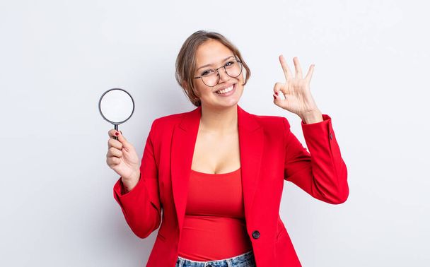 hispanic pretty woman feeling happy, showing approval with okay gesture. magnifying glass concept - 写真・画像