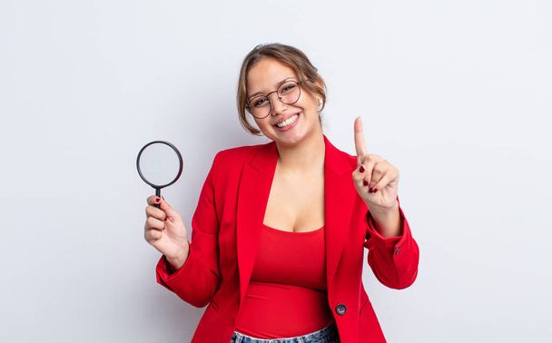 hispanic pretty woman smiling and looking friendly, showing number one. magnifying glass concept - Zdjęcie, obraz