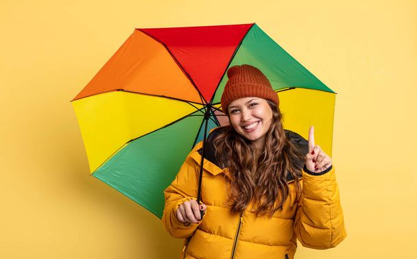 hispanic pretty woman smiling and looking friendly, showing number one. umbrella concept - Photo, Image