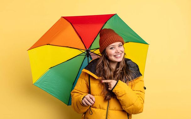hispanic pretty woman looking excited and surprised pointing to the side. umbrella concept - Φωτογραφία, εικόνα