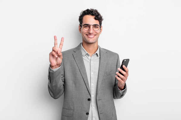 hispanic handsome man smiling and looking friendly, showing number two. business and phone concept - Photo, Image