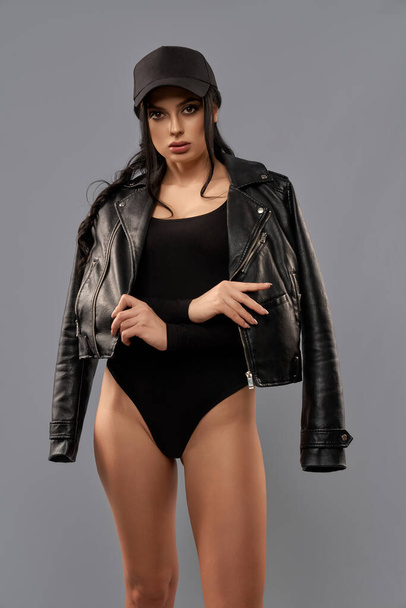 Woman in black bodysuit, cap and leather jacket in studio - Foto, imagen
