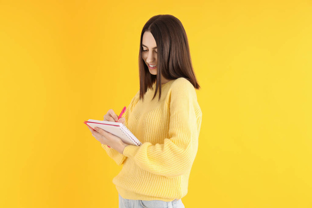 Atrakcyjna dziewczyna z notatnikiem na żółtym tle - Zdjęcie, obraz