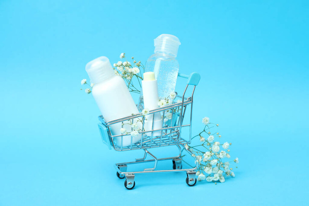 Shop trolley with cosmetics on blue background - Foto, afbeelding