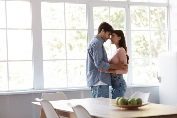 Satisfied cheerful young husband and wife dancing and hugging together in kitchen interior - Foto, Bild