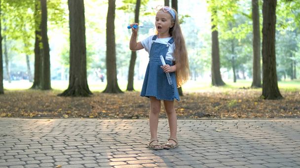 Little happy child girl blowing soap bubbles outdoors in summer park - Foto, afbeelding
