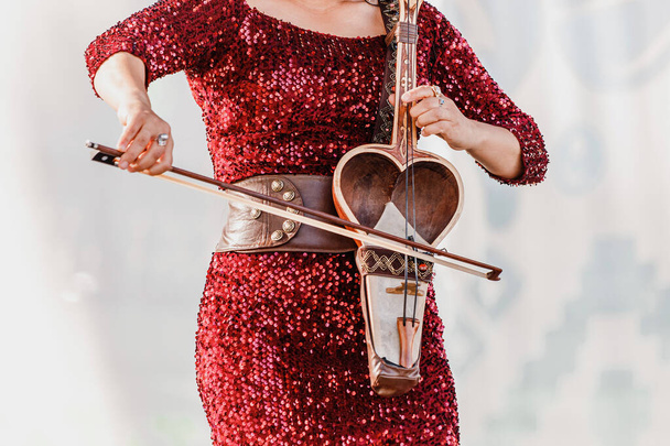 μια γυναίκα παίζει στη σκηνή ενός λαϊκού φεστιβάλ και παίζει το kobyz, ένα έγχορδο τουρκικό όργανο - Φωτογραφία, εικόνα