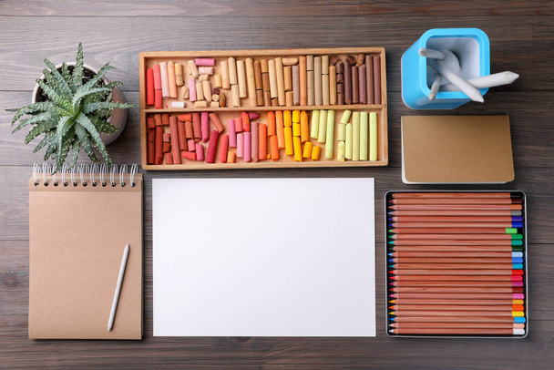 Blank sheet of paper, colorful chalk pastels and drawing pencils on wooden table, flat lay. Modern artist's workplace - Fotografie, Obrázek