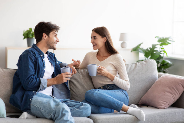 Веселі коханці молодий європейський хлопець і леді, з чашками гарячого напою розмова в інтер'єрі кімнати
 - Фото, зображення