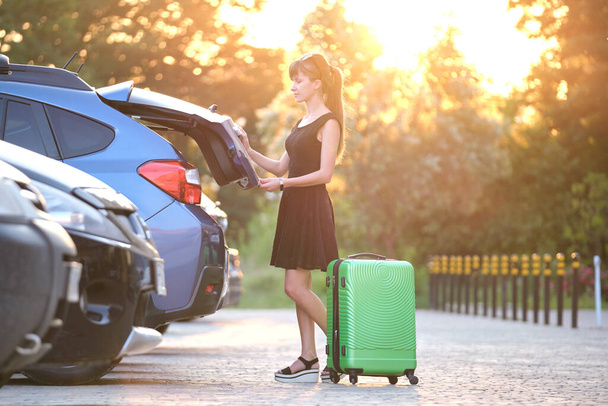 Young female driver taking out luggage suitcase bag out of her car. Travelling and vacations concept - Foto, afbeelding