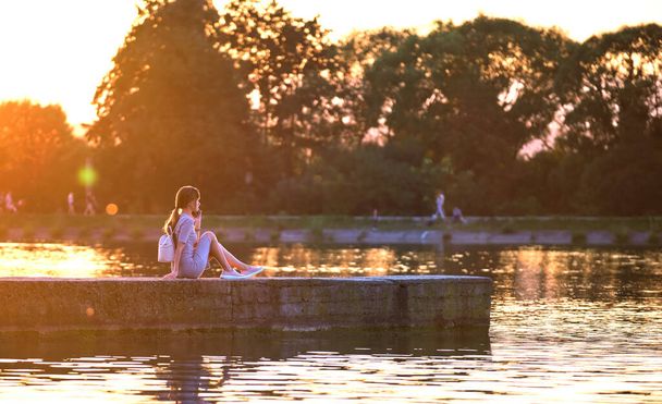 Jovem mulher em roupa casual relaxante no lado do lago na noite quente. férias de verão e conceito de viagem - Foto, Imagem
