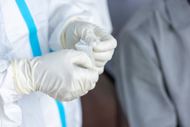 Az orvos PPE öltönyben, orvos használ egy teszt koronavírus (covid-19) segítségével ATK teszt készlet orrkendő. - Fotó, kép