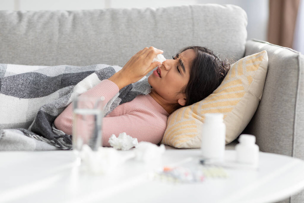 Despaired upset millennial indian woman covered with blanket, suffers from flu blows nose in napkin - Photo, Image