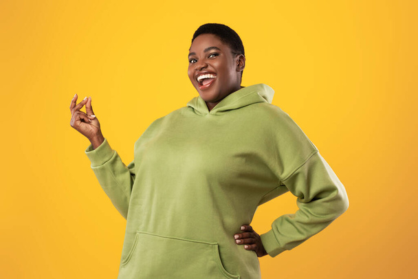 Радісна надмірна вага чорна жінка забиває пальці над стоячим жовтим тлом
 - Фото, зображення