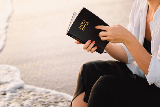 クリスチャンの女性は聖書を手に持っています。美しい日没の間に海で聖書を読む - 写真・画像