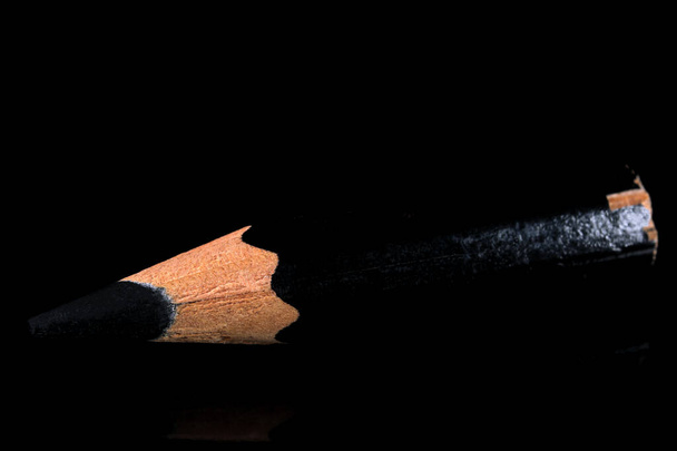 Ένα παλιό μικρό χρησιμοποιημένο αιχμηρό μαύρο ξύλινο μολύβι σχιστόλιθου βρίσκεται σε ένα μαύρο καθρεφτιζόμενο φόντο γκρο πλαν - Φωτογραφία, εικόνα