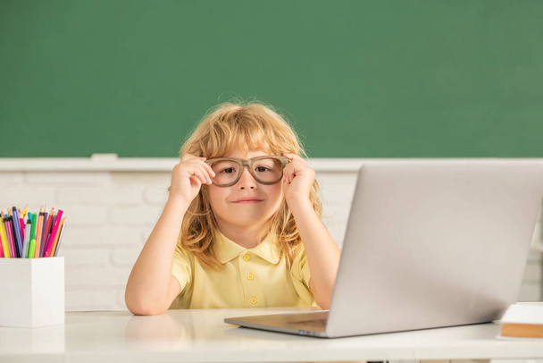ガラスの中の子供の男の子はラップトップと学校の教室でオンラインで勉強します,知識の日 - 写真・画像