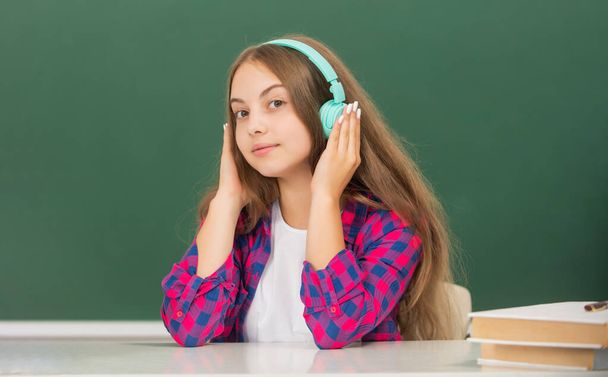 smiling kid with earphones at blackboard, audio accessory - Photo, Image