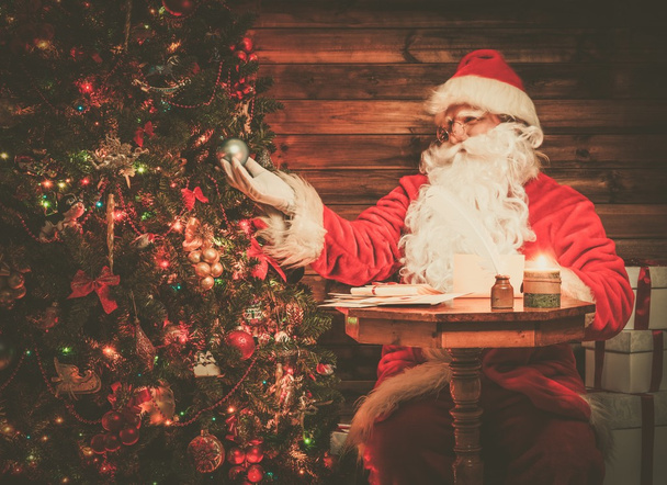 Père Noël à l'intérieur de la maison en bois regardant arbre de Noël décoré
 - Photo, image