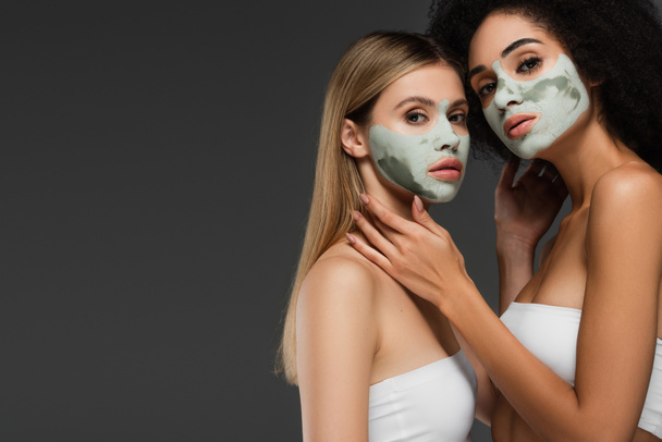 multiethnic woman in white tops and clay masks posing isolated on grey - Photo, Image