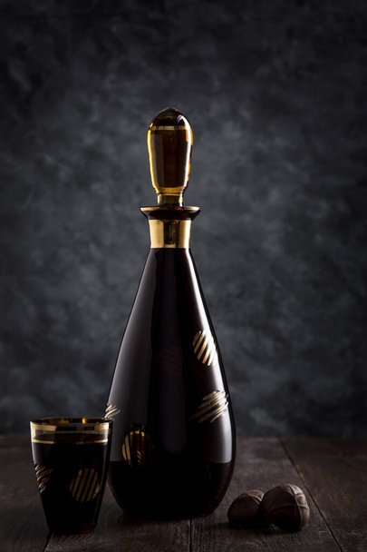 Liqueur in a glass, decanter and chocolates on a dark background. - Foto, imagen