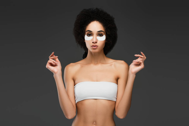 slim african american woman in white top and eye patches looking at camera isolated on grey - Fotografie, Obrázek
