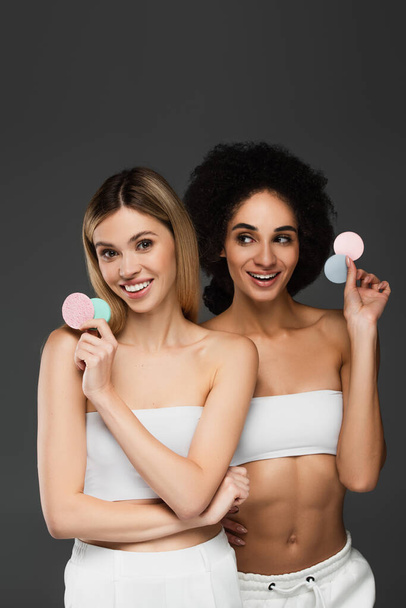 jeunes et minces femmes multiethniques posant avec des éponges cosmétiques isolées sur du gris - Photo, image