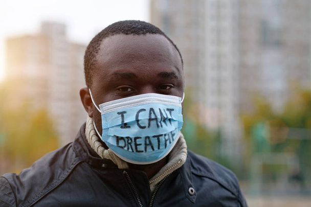 Hombre afroamericano activista en máscara médica con una inscripción NO PUEDO BREATHE mira a la cámara. Black Lives Matter, BLM, discriminación racial, protestas masivas en Estados Unidos - Foto, imagen