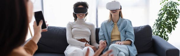 interracial lesbian couple in vr headsets smiling near blurred psychologist with smartphone, banner - Fotoğraf, Görsel