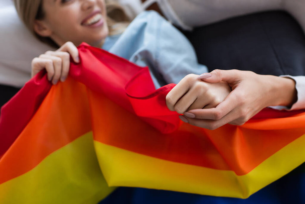 cropped view of lesbian woman holding hand of blurred girlfriend with lgbt flag - Fotografie, Obrázek