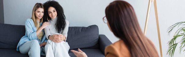размытый психолог разговаривает с улыбающейся многонациональной лесбийской парой в консультационной, баннер - Фото, изображение