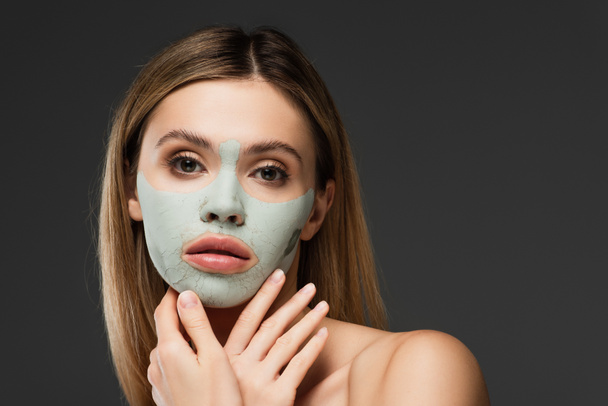 young woman holding hands near face with clay mask isolated on grey - Photo, Image