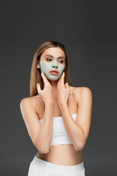 woman in white top touching clay mask on face isolated on grey - Foto, Imagen