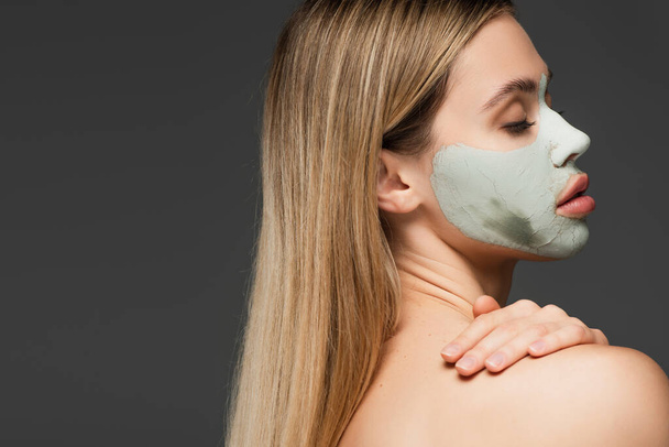 young woman with closed eyes and clay mask on face posing isolated on grey - Fotografie, Obrázek