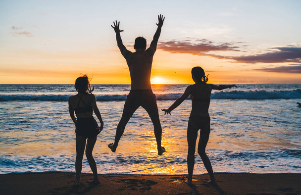 Back view of unrecognizable barefoot family enjoying summer holidays together and having fun on sandy beach near waving sea in evening time on Bali - Фото, изображение