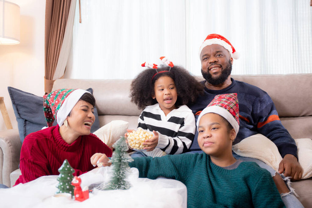 Felicidad Africana familia mamá y papá e hija viendo la televisión y riendo con diversión y disfrute en la sala de estar en casa, ocio familiar con televisión para cómodo en el día de Navidad. - Foto, Imagen
